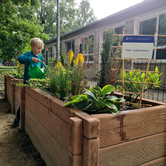 Dieťa polieva kvety v nových vyvýšených záhonoch MC Úsmev